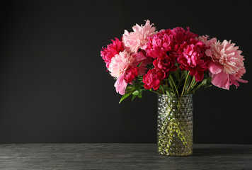 Glass vase with bouquet of beautiful peonies on wooden table against black background, space for text