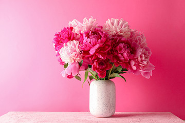 Vase with bouquet of beautiful peonies on pink table against color background, space for text