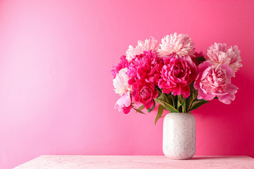 Vase with bouquet of beautiful peonies on pink table against color background, space for text