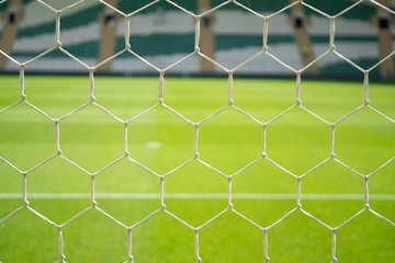Close up detail of a soccer net against green grass and blur stadium seats