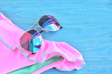 Colorful aviator sunglasses and neon trendy bikini with selective focus on wooden textured...