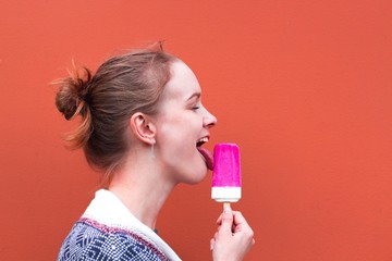 Beautiful and young girl eats a pink hue ice cream and enjoys. She closed her eyes from pleasure and licked his tongue. She stands against a pink shade.