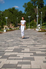Fototapeta na wymiar Young beautiful brunette girl in white jeans and t-shirt walking in summer park