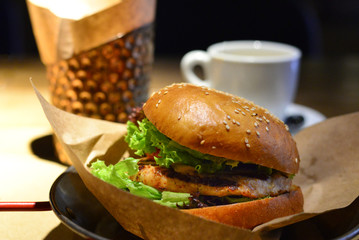 Delicious tasty burger with beef, tomatoes, salad and sauce on wooden table and black background.  Space for text or design.