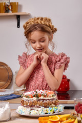 Little girl is making a homemade cake with an easy recipe at kitchen against a white wall with shelves on it.