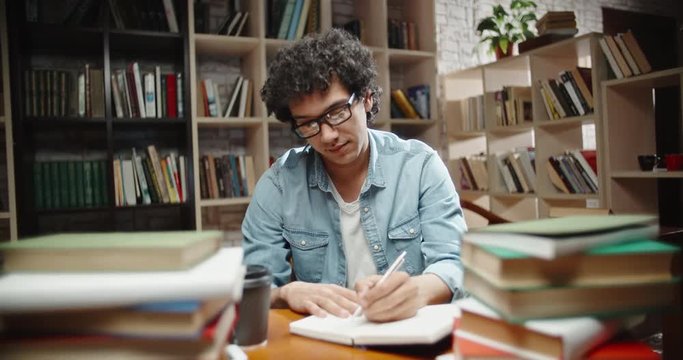 Asian guy looking at camera while studying. Student is making a project, doing research for it, preparing for exam - close up portrait 4k