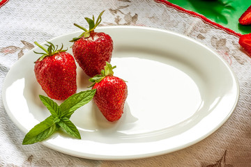 Three juicy fresh strawberries with a leaf of mint