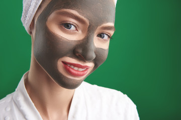 Charming girl with clay facial mask standing against green background