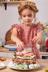 Little girl is making a homemade cake with an easy recipe at kitchen against a white wall with shelves on it.