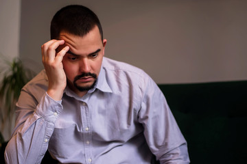 Stressed middle-aged man in wrinkled shirt sitting indoor with raised eyebrow having put head on hand. Thoughts, job issues, depression, business problems concept. Midlife crisis. Room for copy text