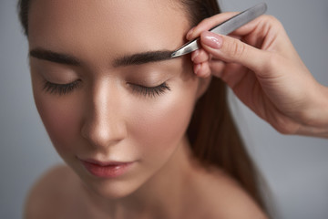 Fototapeta premium Relaxed girl is having brows brushed isolated on grey background