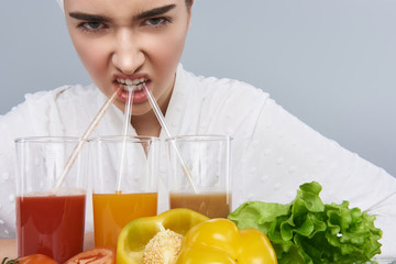 Woman actively sipping three vegetable drinks against grey background
