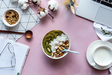 Healthy breakfast bowl milk laptop and organizer on pink table background concept, morning meal at work in home office, natural nutrition food with computer concept, freelancer workplace, top view
