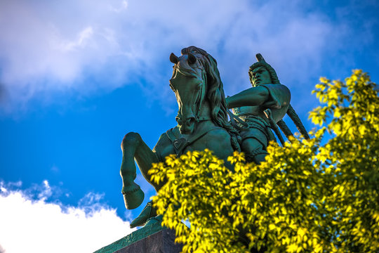 Majestic bronze green monument to Salawat Yulaev, close-up shot through spring foliage on a bright summer day. Folk hero on a horse with whip in his hand. Salavat Yulayev, Ufa, Bashkortostan, Russia.