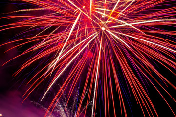 Flickering lights are a bright salute of abstract red yellow blue cyan luminescent traces of petals on long exposure on a night black sky background. Fireworks on the day of the city of Ufa, Russia.