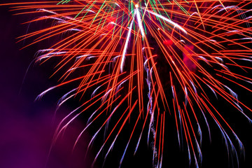 Fototapeta premium Flickering lights are a bright salute of abstract red yellow blue cyan luminescent traces of petals on long exposure on a night black sky background. Fireworks on the day of the city of Ufa, Russia.