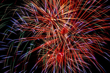 Flickering lights are a bright salute of abstract red yellow blue cyan luminescent traces of petals on long exposure on a night black sky background. Fireworks on the day of the city of Ufa, Russia.