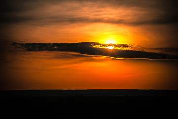 Cloud silhouette on a bright colorful orange sky hiding the yellow sun over the black steppe plain. Ufa, Bashkortostan, Russia.