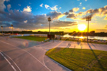 People walk, rollerblading and biking in the biathlon stadium at sunset in the bright yellow rays of the sun on the banks of the river. Biathlon Stadium, Ufa, Bashkortostan, Russia.