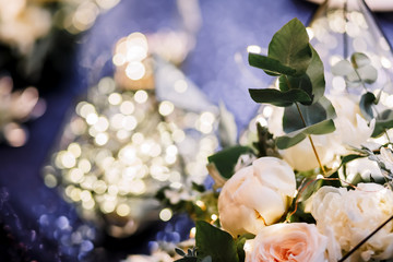 Table decoration with fresh flowers in pastel colors. Elegant dining table in peach-lilac color. Luxurious composition. Indoors wedding. Beautiful table setting. Garland in a glass flask.