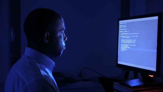 Portrait of african american man programmer coding network security software. Hacker typing code on computer screen in dark office at night