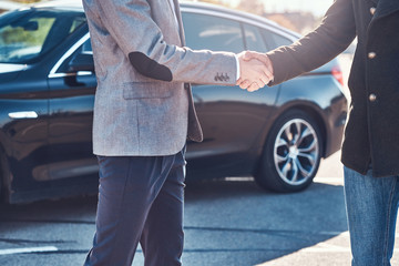 Photo of two smart elegant men, which have a deal about car. They are doing handshake.