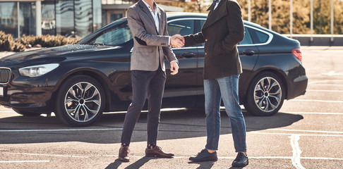 Photo of two smart elegant men, which have a deal about car. They are doing handshake.