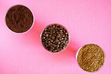 A variety of coffee - three types in one picture: roasted beans, ground and instant granulated. In round glass bowls on a pink background. Diagonal