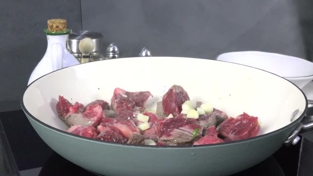 Adding chopped garlic and onion to simmering cubes of beef