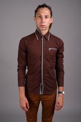 Young man with dreadlocks wearing brown shirt against gray backg