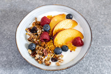 Top view selective focus of granola with greek yogurt fresh peach, blueberry, raspberry on the table - healthy breakfast