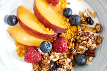 Top view selective focus of granola with greek yogurt fresh peach, blueberry, raspberry on the table - healthy breakfast