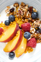 Top view selective focus of granola with greek yogurt fresh peach, blueberry, raspberry on the table - healthy breakfast