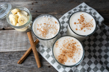 Banana smothie or milkshake with cinnamon on wood background