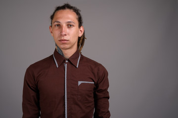 Young man with dreadlocks wearing brown shirt against gray backg