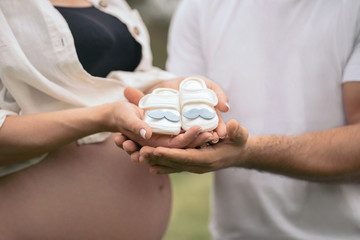 happy pregnant couple holding baby boy shoes in hands outdoor; closeup portrait. pregnancy and...