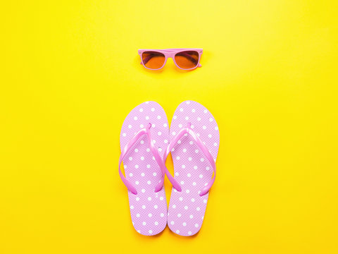 Summer flat lay. Beach accessories pink flip flops and sunglasses on yellow background. Summer trevel and vacation concept