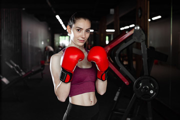 Young pretty woman in red boxing gloves on a background of the gym. Female boxer. Close up portrait of fighter girl. Winner.