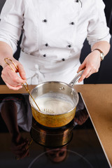 Close-up of chef mixing milk for cake for baking cake and making chocolate. Hands cook stir milk whisk in a metal bucket warming it on the stove