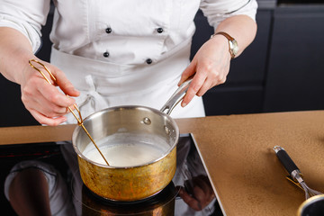 Close-up of chef mixing milk for cake for baking cake and making chocolate. Hands cook stir milk whisk in a metal bucket warming it on the stove