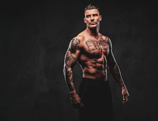 Fototapeta na wymiar A tattooed muscular shirtless man with stylish hair posing at the camera on a dark background.