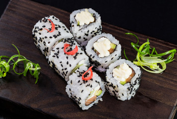 Japanese traditional rolls with seafood and fish, vegetables, on a black background.