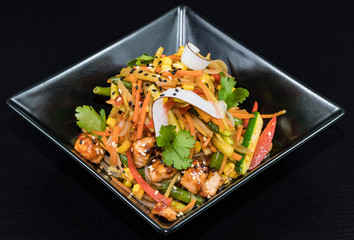 Asian noodles with vegetables and meat on a black background.