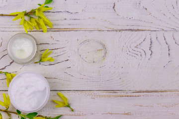Jar of moisturizer cream with yellow forsythia blossoms on white wooden background. Top view