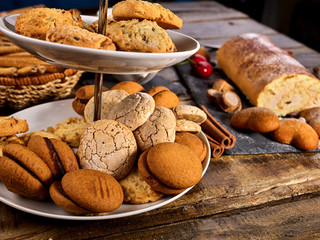 Oatmeal and nut cookies and sand biscuit on tier cake stand with straw pastry in basket on kitchen on wooden table in rustic natural style. Top view of two cups of tea on wooden table. Perfect product