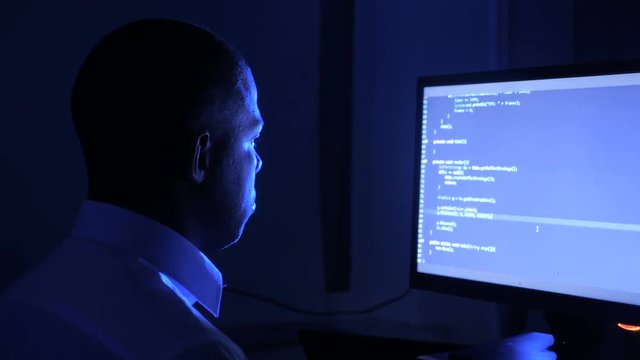 Portrait of african american man programmer coding network security software. Hacker typing code on computer screen in dark office at night