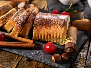 Sand cookies heart shape, rolled cake with cherry and cinnamon stick, coffee cups on kitchen on wooden table in village style. Useful for digestion. Sunlight in kitchen.