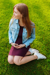 Fototapeta premium Happy young pregnant woman sitting in the park on the lawn,