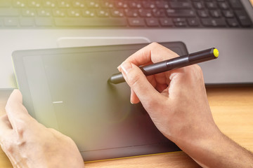 Illustrator using a graphics tablet. Woman's retoucher's hands using laptop and drawing tablet.
