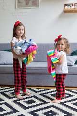 Two little girls sit in a room on the floor and play with clothes . the cleaning in the house. the concept of parenting